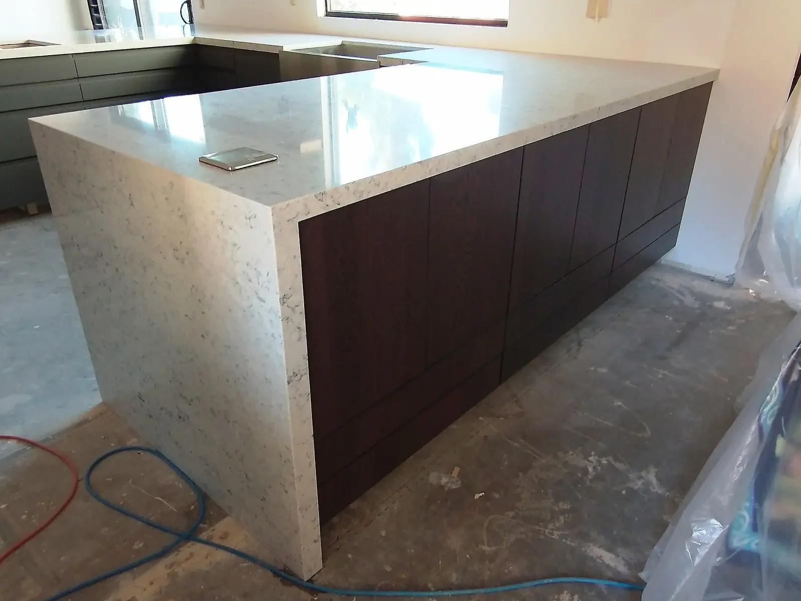 A kitchen island with a quartz waterfall countertop over dark cabinets, during a remodel