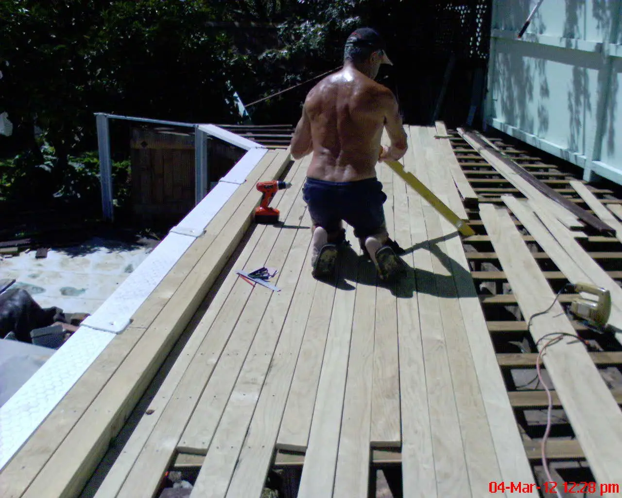 A worker fitting new boards onto a wooden deck frame