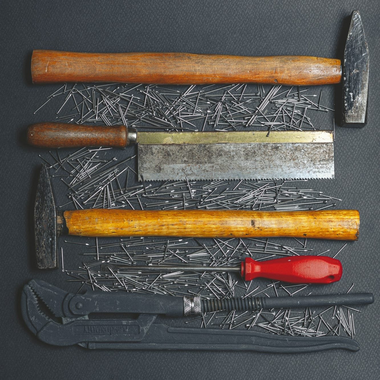 Hammers, hand saw, screwdriver and pipe wrench laid out on a dark workbench