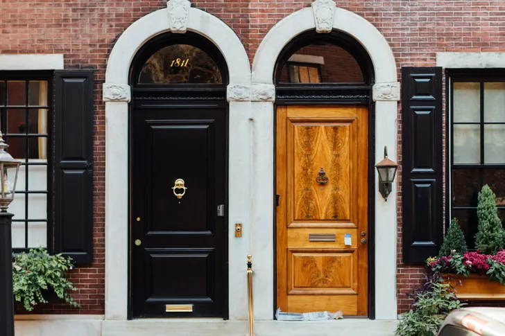 Two front doors, one black and one wood, at a brick townhouse entry