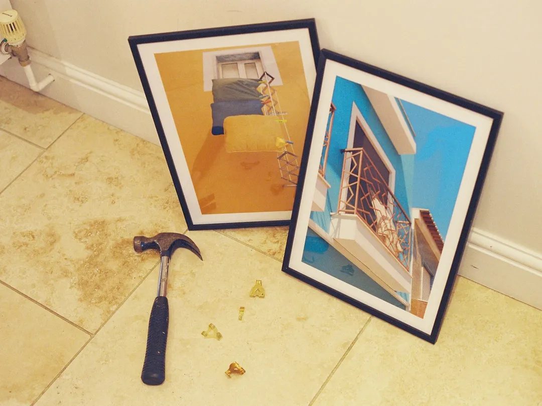 Two framed prints, a hammer and brass picture hooks on a tiled floor