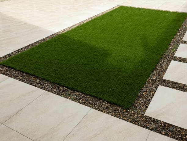 Rectangle of artificial grass bordered by gravel and large stone pavers