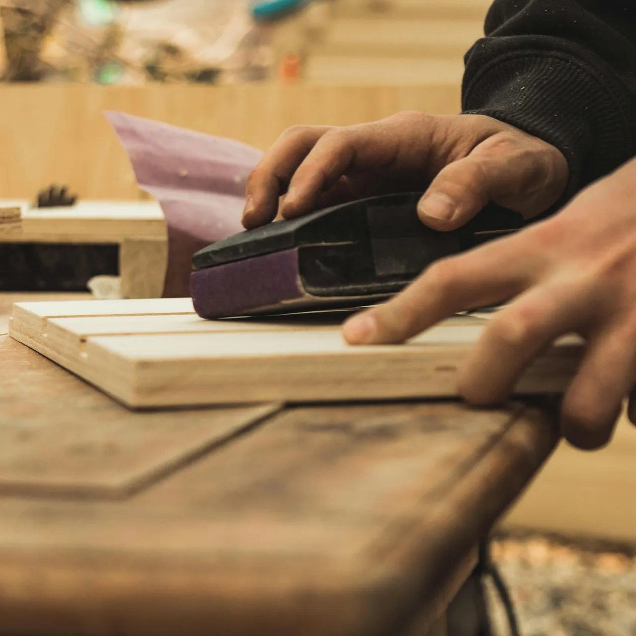 Hands sanding a wooden board on a workbench