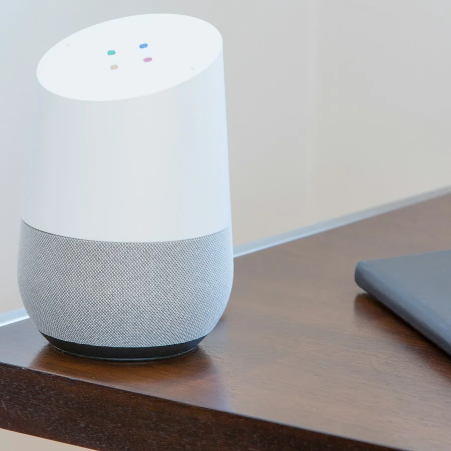 Smart speaker on a wooden side table beside a notebook