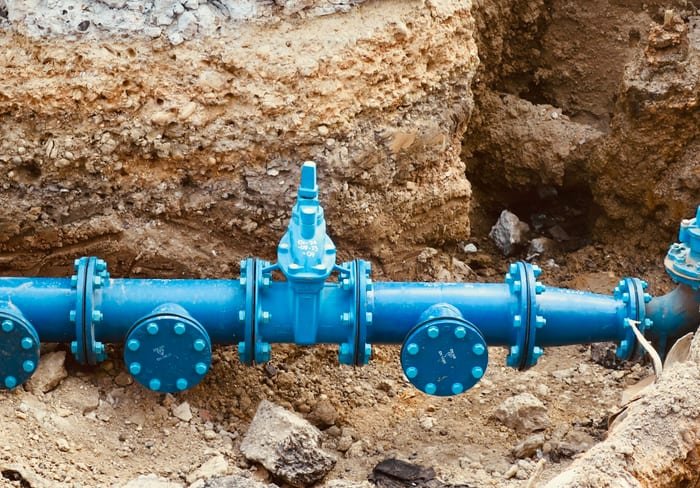 Blue water pipe with valves exposed in a dug-out trench