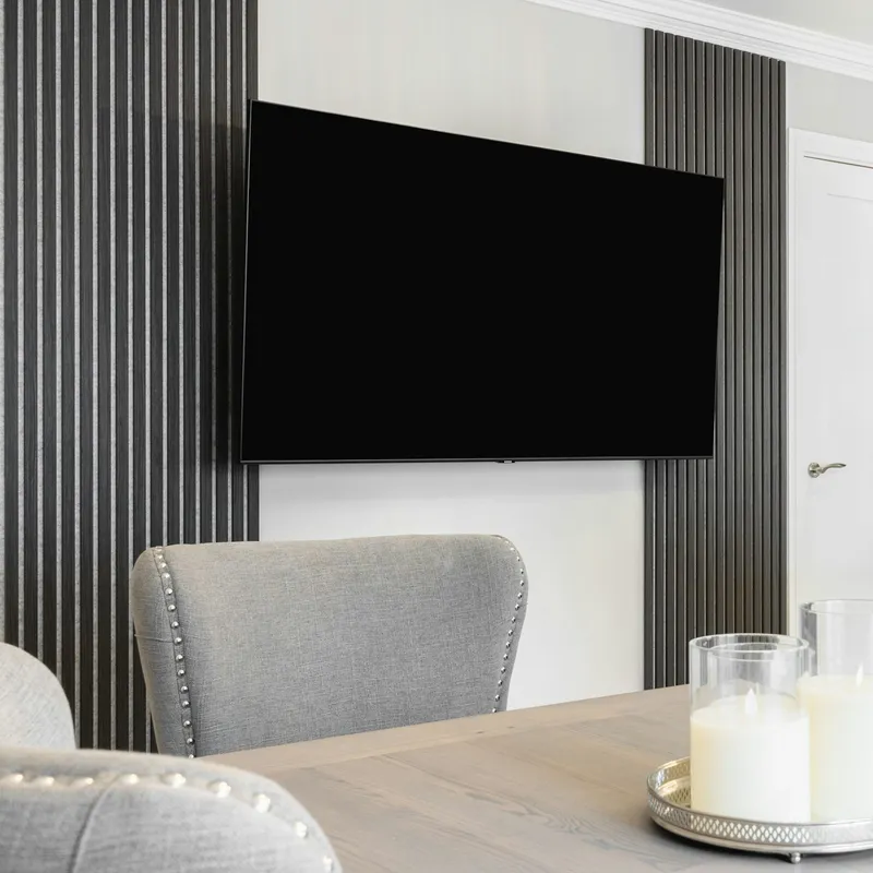 Flat-screen TV on a wall mount between slatted panels above a dining table