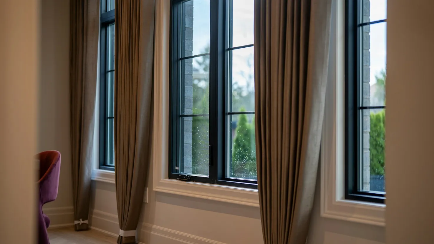 Floor-length taupe drapes hanging beside tall black-framed windows