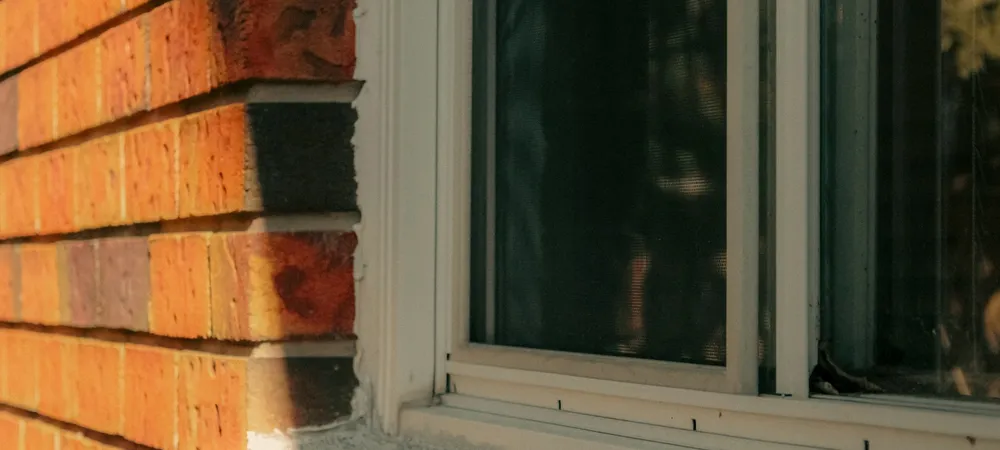 Joint where a white window frame meets a red brick wall
