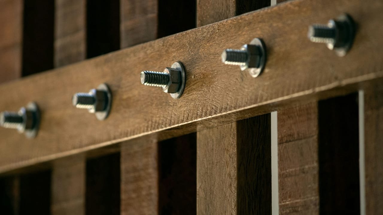 Row of bolts fastened through a wooden rail on a wood frame