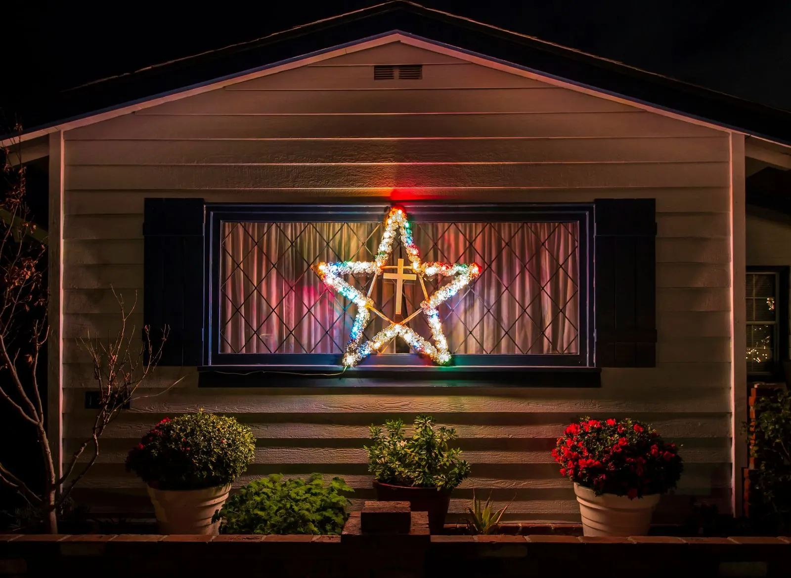 Lighted Christmas star in the front window of a wood-sided cottage at night