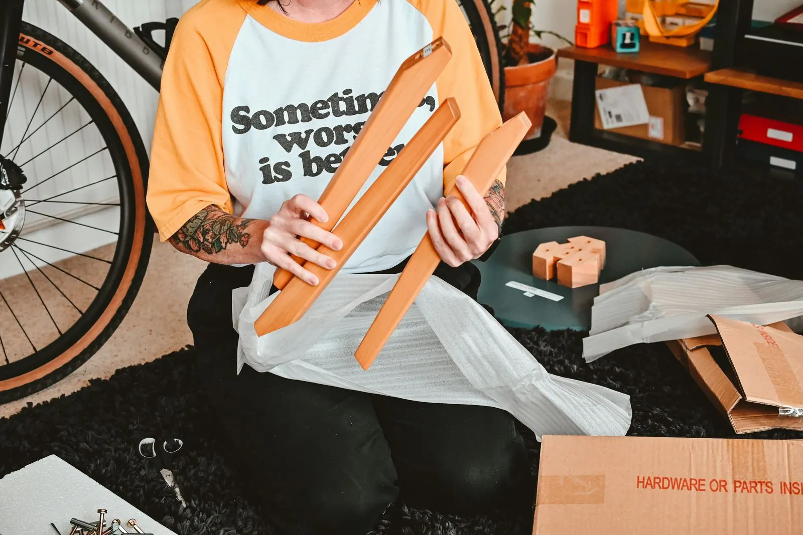 Person unpacking flat-pack furniture parts from foam wrap, with the hardware box on the floor