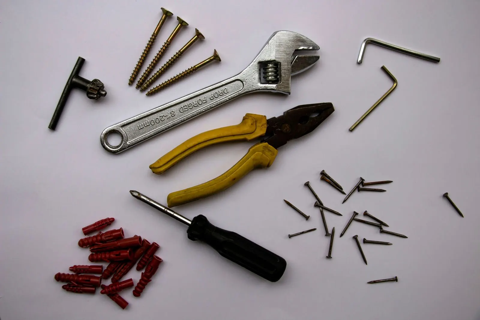 Allen keys, screws, wall anchors, a screwdriver, pliers and an adjustable wrench laid out on a white surface
